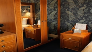 Ein Hotelzimmer mit Holzschrank, Bett mit Nachtkästchen und Spiegel.