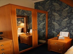 A bedroom with a wooden wardrobe, a bedside table with a lamp, a nightstand, and a mirror. - Standard Double Room (Derby)