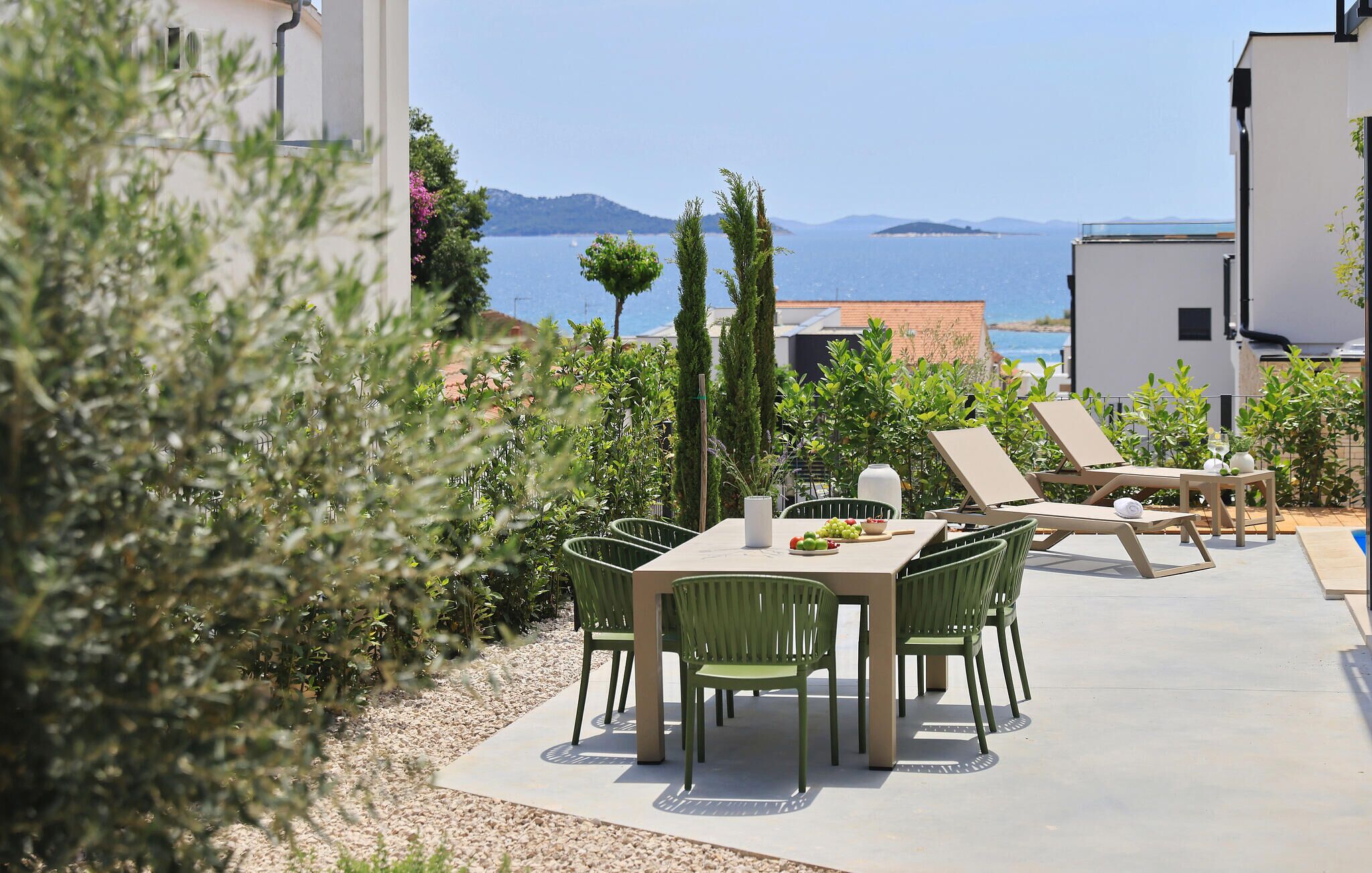 An outdoor patio with a table and chairs, a pool, and a view of the sea and mountains.