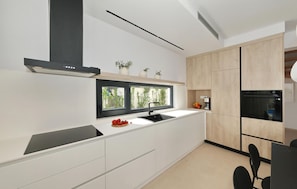A modern kitchen with a black range hood, a window with a view, wooden cabinets, and a black countertop. - Luxurious home in Pakostane (Pakostane)
