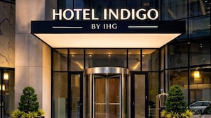 L’entrée d’un hôtel, avec une porte tournante, une façade en verre et l’inscription « HOTEL INDIGO BY IHG » au-dessus.