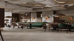 Ein modernes Restaurantambiente mit gepolsterten grünen Sitzbänken, Esstischen und Pendelleuchten.