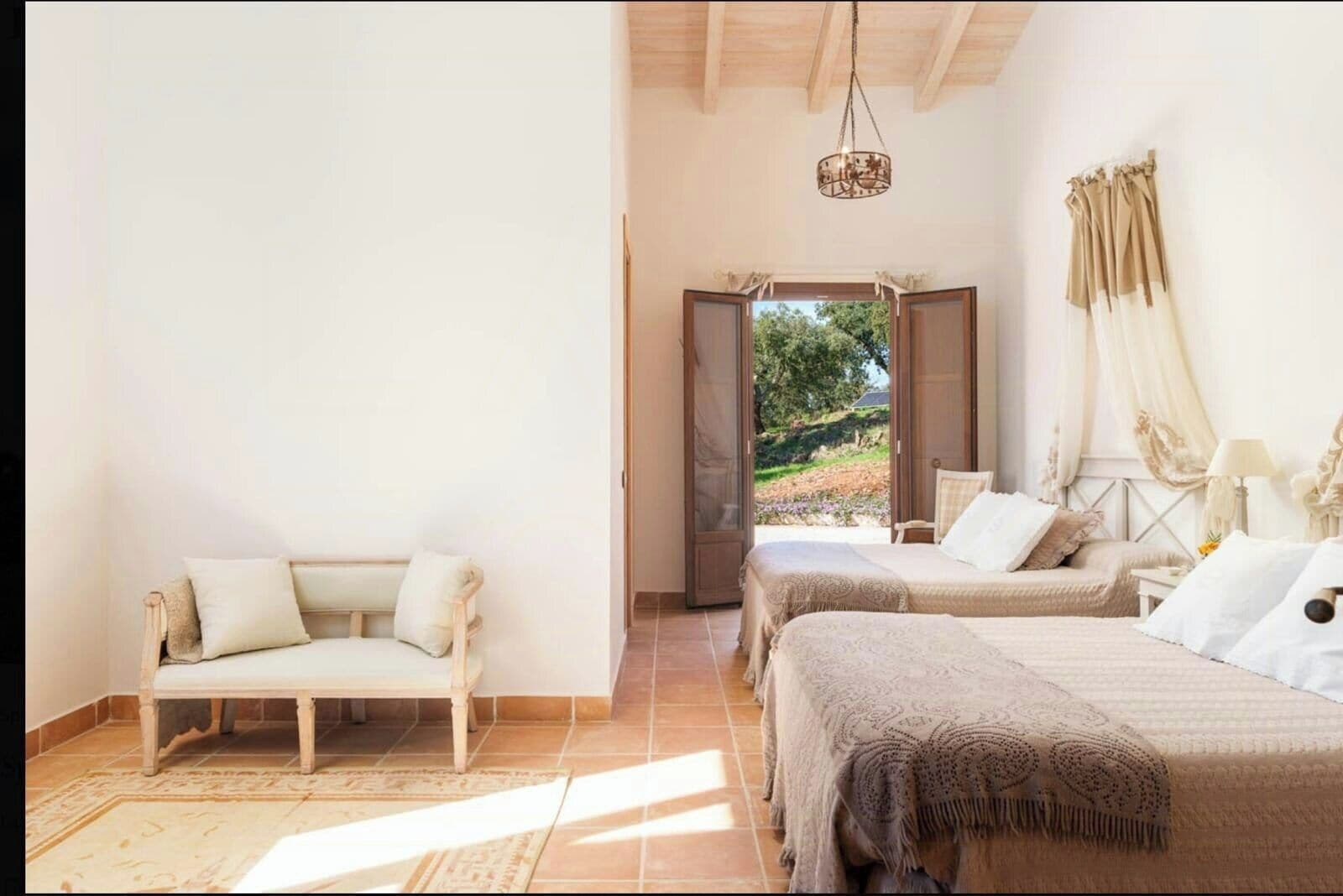 A bedroom with a sofa, two beds, a chandelier, and a view through an open door.