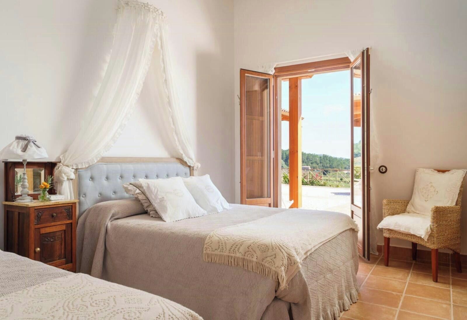 A bedroom with a bed, a nightstand, a chair, and an open door leading to a balcony.