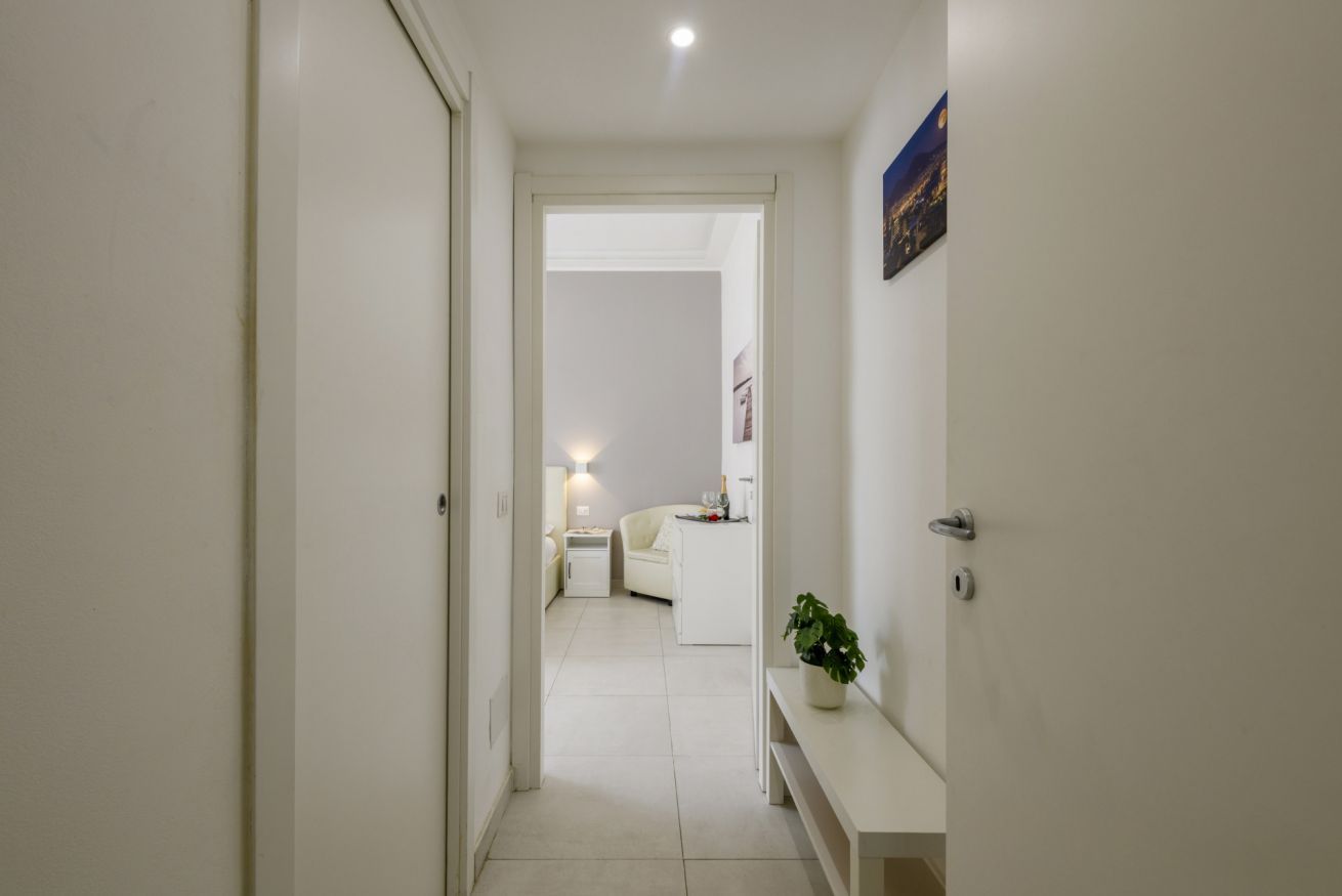 Un couloir menant à une chambre à coucher équipée d’un lit, d’une table de chevet et d’une petite table de nuit.