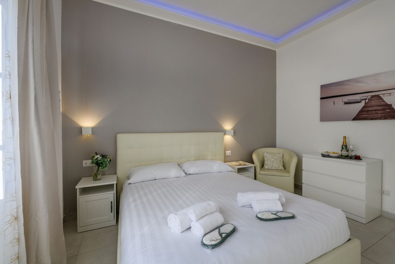 Ein Hotelzimmer mit Bett, Nachttischen, einem Sessel, einem Schminktisch und einem Bild an der Wand.