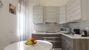 A modern kitchen with a white dining table, clear chairs, and a fruit bowl. - VIA TAGIURA 25/27 - For Work and Leisure (Milan)