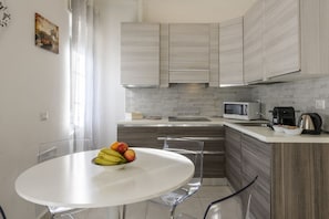 A modern kitchen with a white dining table, clear chairs, and a fruit bowl. - VIA TAGIURA 25/27 - For Work and Leisure (Milan)