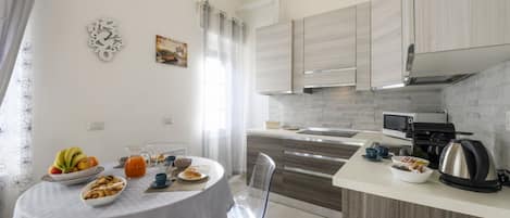 A modern kitchen with a dining area, featuring a round table with breakfast items, a coffee machine, and a kettle.