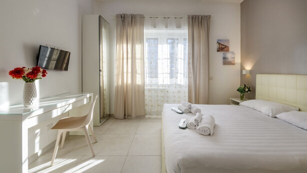 A hotel room with a bed, a desk, a chair, a TV, and a window with curtains. - VIA TAGIURA 25/27 - For Work and Leisure (Milan)