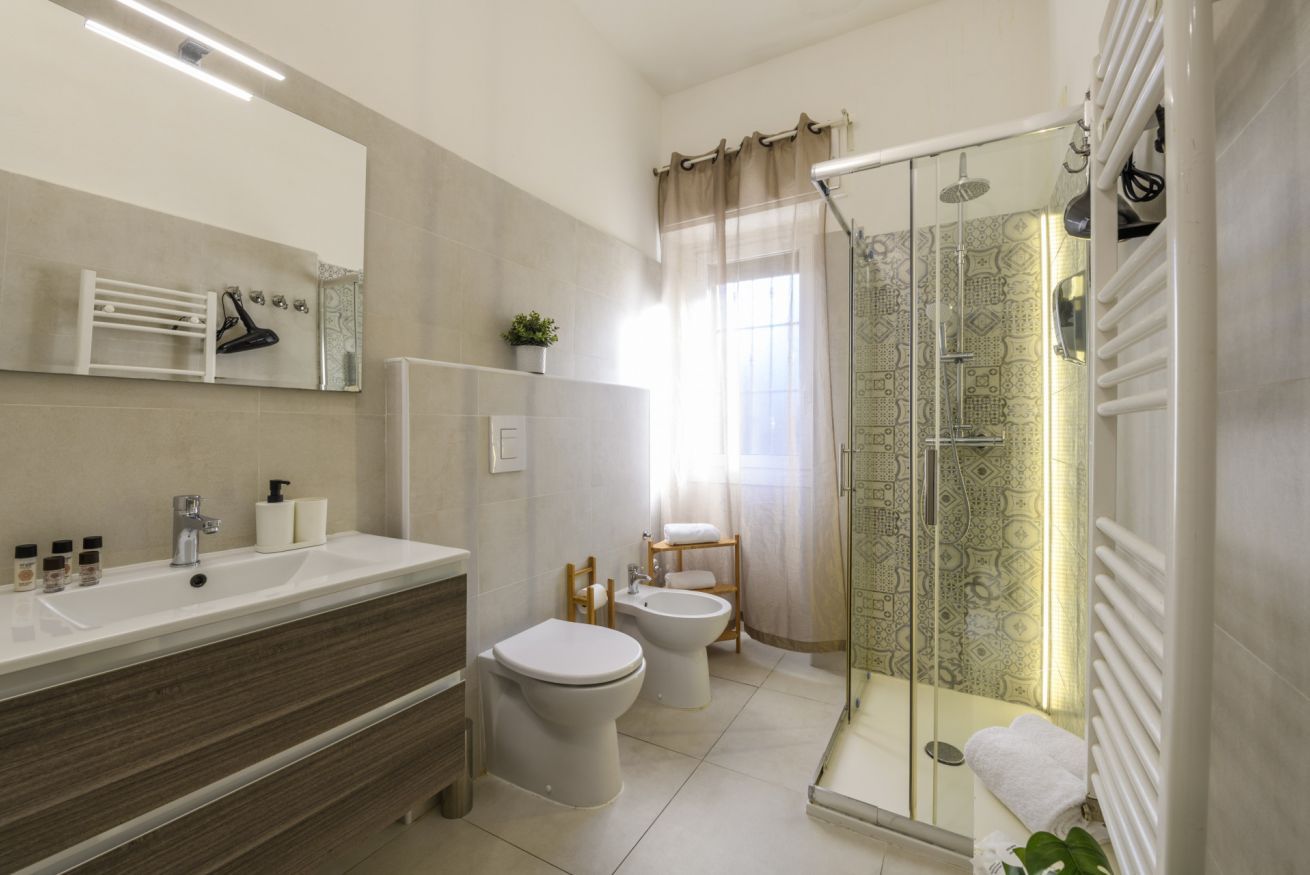 Een moderne badkamer met een grote spiegel, een wastafel, een toilet, een douchetoilet en een douche met glazen wanden.