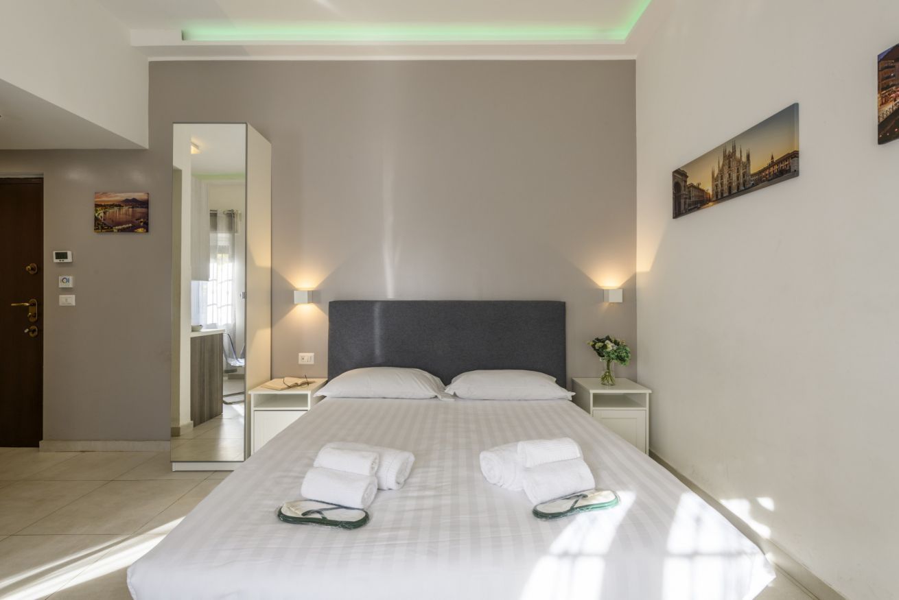 A hotel room with a large bed, two bedside tables with lamps, a mirror, and artwork on the walls.