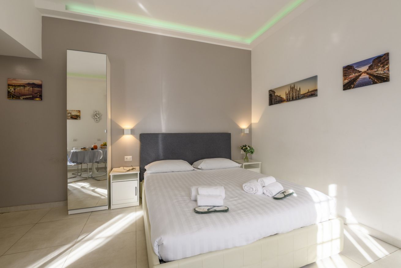 A modern hotel room with a large bed, a mirror, bedside lamps, and artwork on the walls.