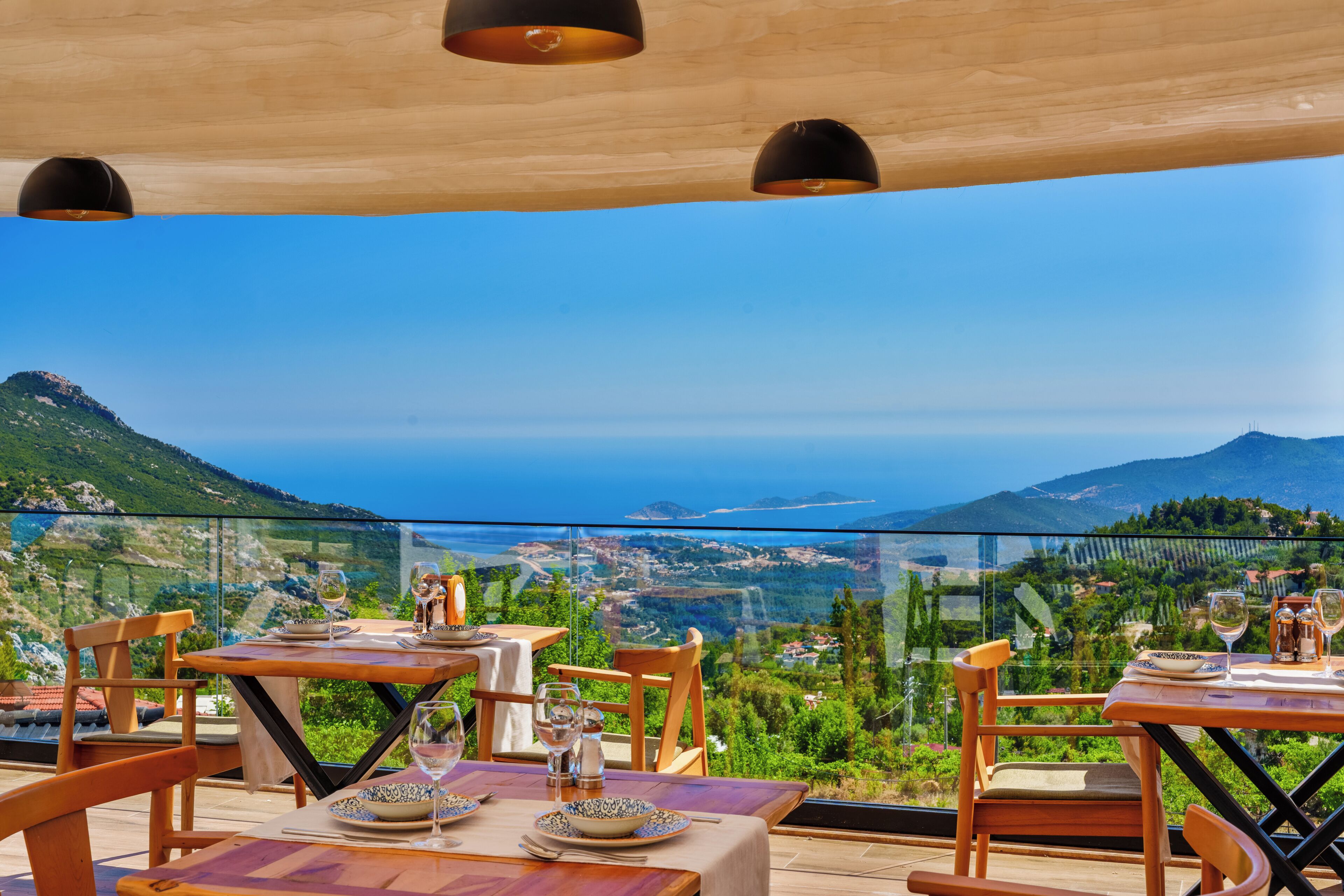 Un espace repas avec des tables et des chaises, une vue sur la mer et les montagnes, et une rambarde en verre.