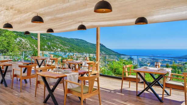 An outdoor dining area with wooden tables and chairs, black pendant lights, and a view of a mountainous landscape. - Turquoise Retreat Wellness & Spa (Kaş)