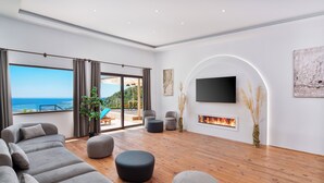A spacious living room with a large sofa, ottomans, a flat-screen TV, and a fireplace. - Turquoise Retreat Wellness & Spa (Kaş)