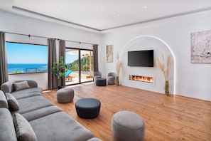 A spacious living room with a large sofa, ottomans, a flat-screen TV, and a fireplace. - Turquoise Retreat Wellness & Spa (Kaş)