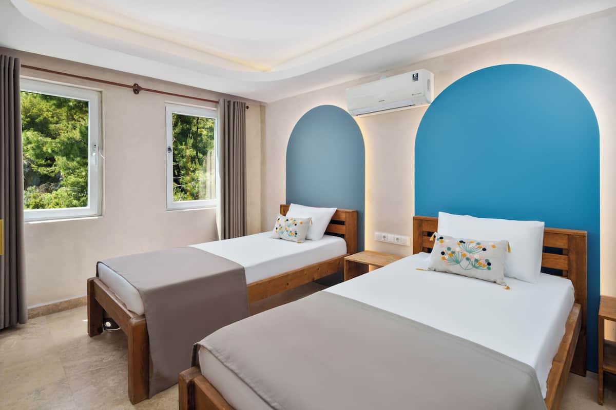 Habitación de hotel con dos camas, una ventana, aire acondicionado y vista a zonas verdes.