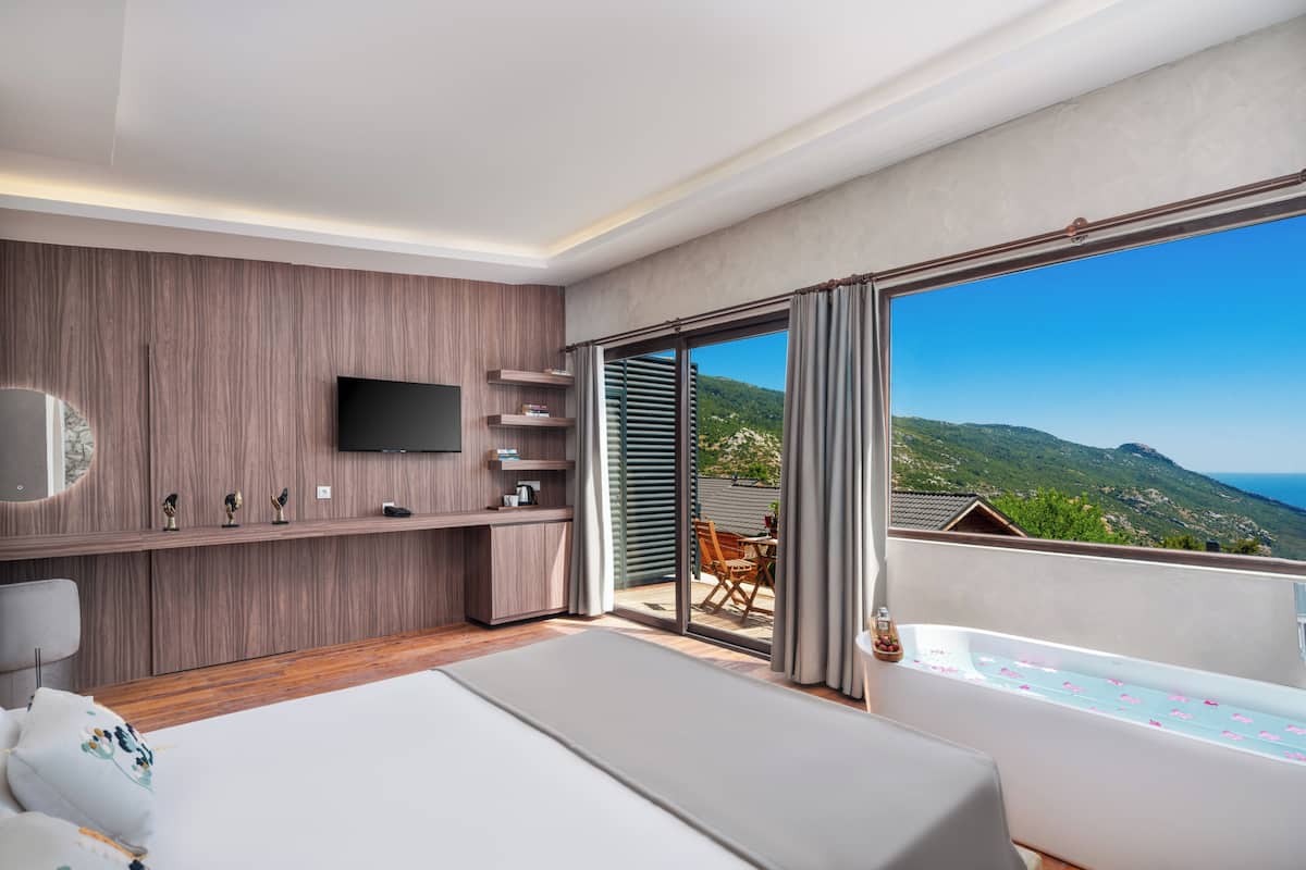 Un dormitorio moderno con una cama grande, un televisor, un balcón con vistas a las colinas y una puerta corredera.