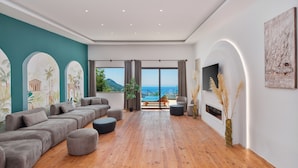 A spacious living room with a large sectional sofa, a flat-screen TV, and a view of the sea. - Turquoise Retreat Wellness & Spa (Kaş)