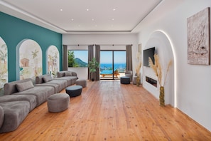 A spacious living room with a large sectional sofa, a flat-screen TV, and a view of the sea. - Turquoise Retreat Wellness & Spa (Kaş)