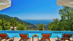 A poolside area with lounge chairs, a table with fruit and drinks, and a view of the sea and hills. - Turquoise Retreat Wellness & Spa (Kaş)