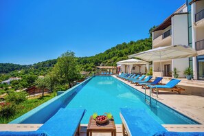 A swimming pool with lounge chairs and umbrellas, surrounded by greenery and a building. - Turquoise Retreat Wellness & Spa (Kaş)