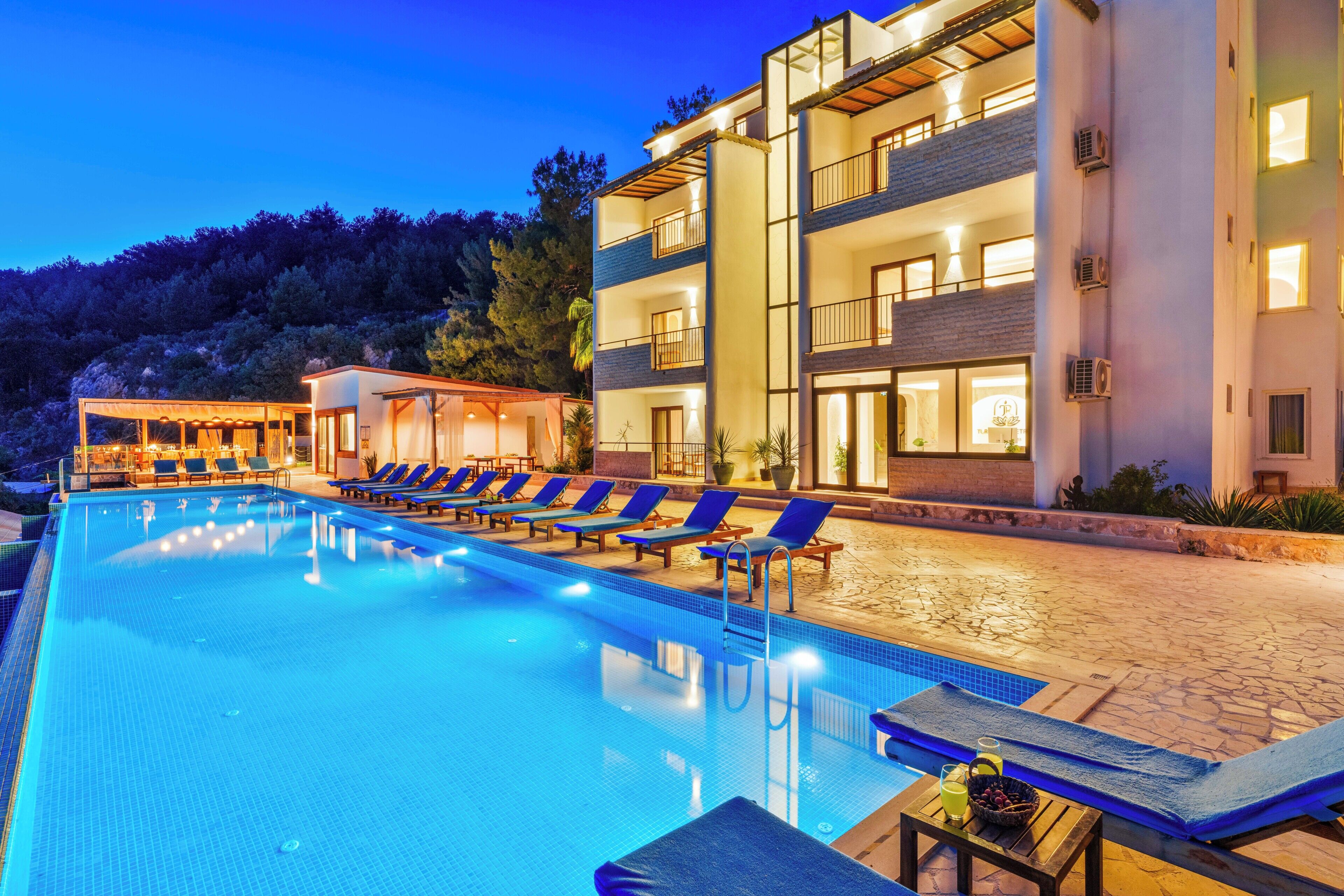 A swimming pool with lounge chairs, a building with balconies, and a mountainous backdrop.