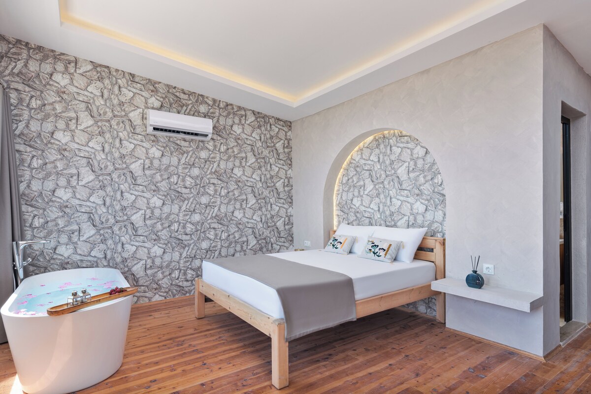 A modern bedroom with a stone wall, a wooden bed, a white bathtub, and a built-in shelf.