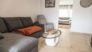 A living room with a grey sofa, a glass coffee table, and a view into another room.