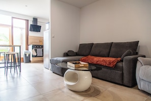 Un saló modern amb un sofà gris, una taula de centre de vidre i una cuina al fons.