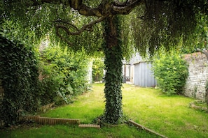 Un jardí amb un arbre, una paret de maó i una caseta.