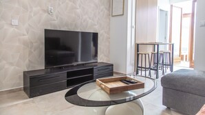 A modern living room with a flat-screen TV, dark entertainment unit, glass coffee table, and a grey sofa. - Cozy House Between the City and the Beach with a Private Garden (Dunkerque)