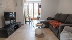 A living room with a TV, a sofa, a coffee table, and a dining area with chairs.