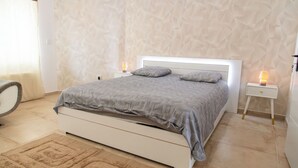 A bedroom with a bed, two bedside tables, a chair, and a patterned wall.