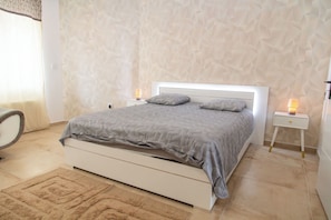 A bedroom with a bed, two bedside tables, a chair, and a patterned wall.