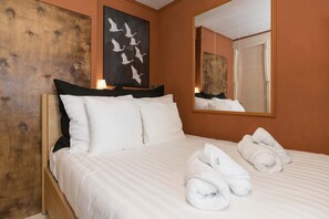 Een hotelkamer met een bed, kussens, een grote spiegel en een kunstwerk aan de muur.