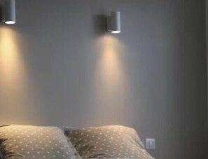 Une pièce avec un lit, deux lampes fixées au mur et un mur uni.