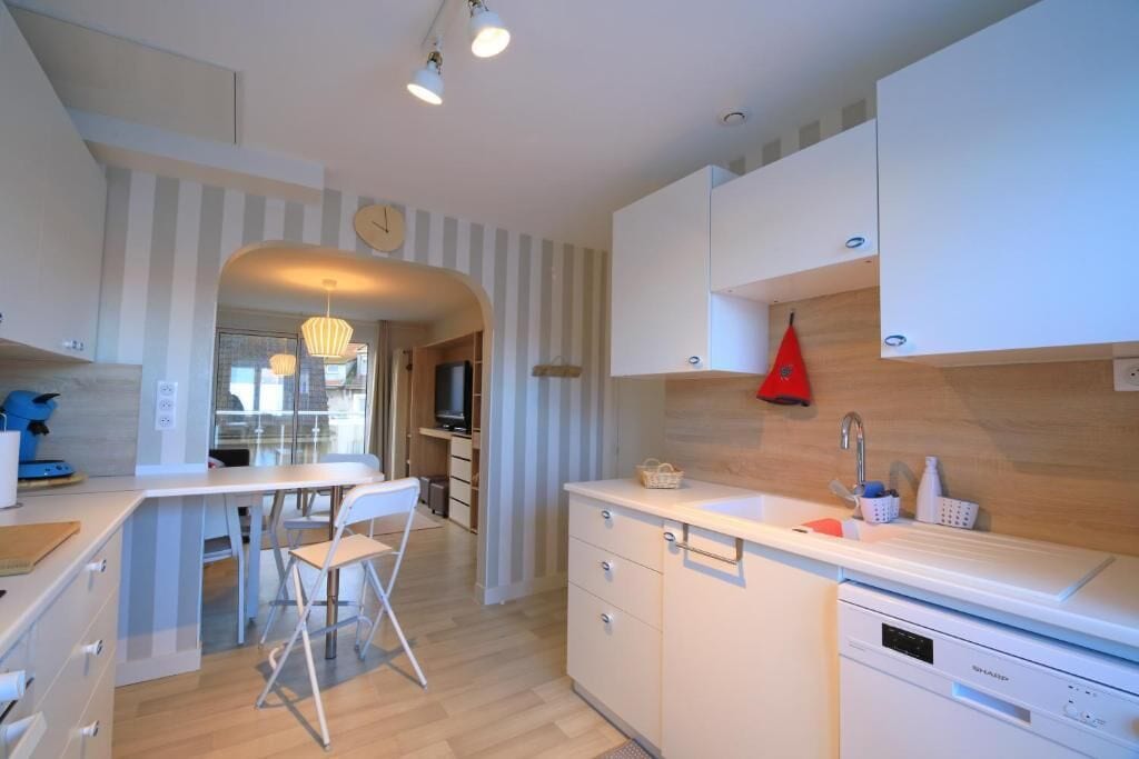 A modern kitchen with white cabinetry, a dining area with a white table and chairs, and a red hanging light.