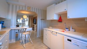 A modern kitchen with white cabinetry, a dining area with a white table and chairs, and a red hanging light. - Les clés de la mer (Le Portel)