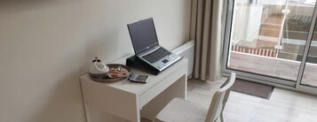 A laptop on a desk with a cup and a plate of pastries, a chair, and a view of a building through a glass door.
