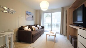 A modern living room with a sofa, a coffee table, a TV, and a dining area. - Les clés de la mer (Le Portel)