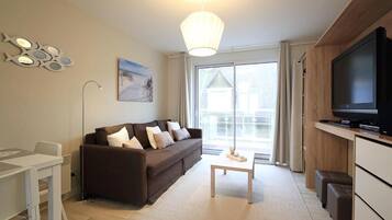 A modern living room with a sofa, a coffee table, a TV, and a dining area.