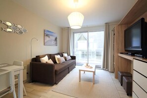 A modern living room with a sofa, a coffee table, a TV, and a dining area. - Les clés de la mer (Le Portel)