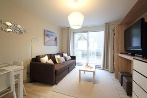 A modern living room with a sofa, a coffee table, a TV, and a dining area.