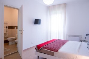 Ein Schlafzimmer mit einem Bett, einem an der Wand befestigten Fernseher und einem durchgegangenen Tür erkennbaren Badezimmer.