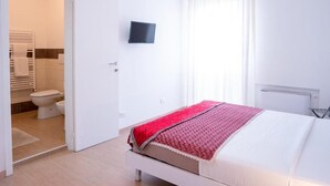 A bedroom with a bed, a television on the wall, and a bathroom visible through an open door. - ca popolo venice (Mestre)