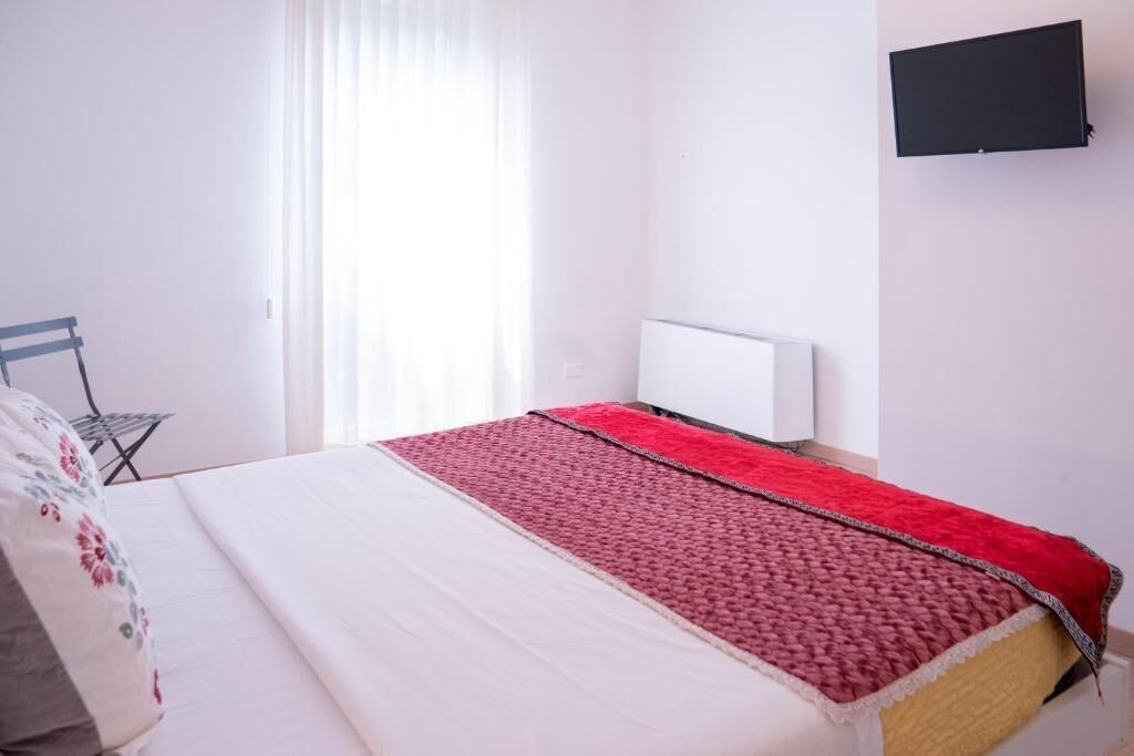 Una camera da letto con un letto, una TV a schermo piatto montata a parete e una finestra con tende.