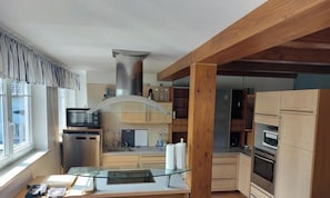 A modern kitchen with a built-in microwave, oven, and dishwasher, wooden cabinets, and a glass-top dining table.