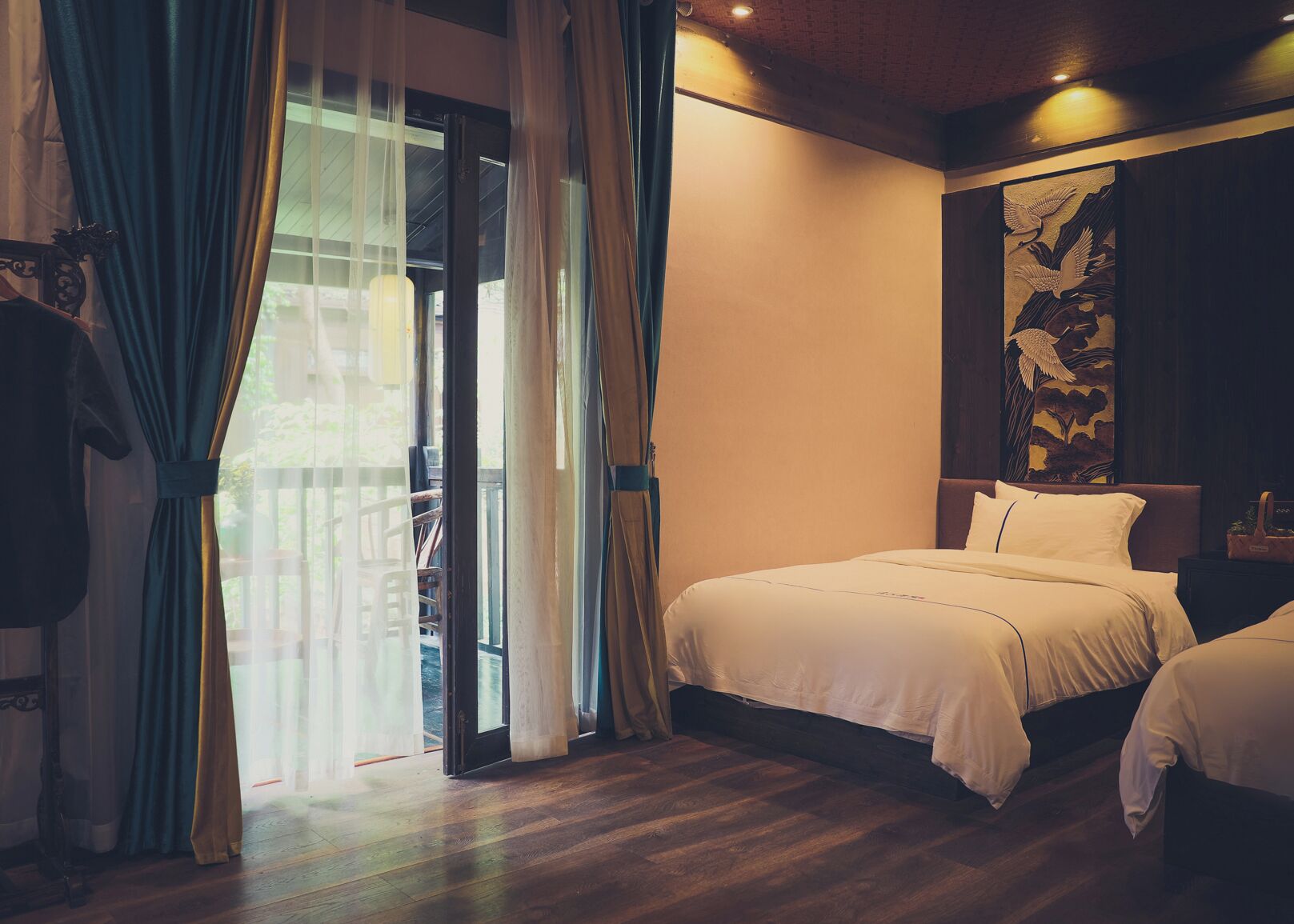 A hotel room with a bed, a nightstand, a painting, and a view through a glass door.